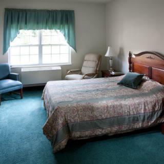 A neatly arranged bedroom with a large bed, window with curtains, and a chair beside a lamp.