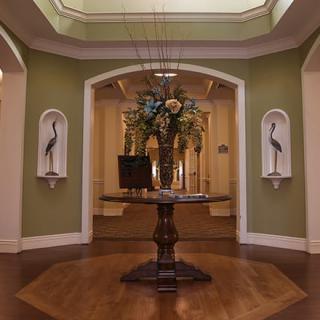 A beautifully decorated foyer featuring a central table with floral arrangements, flanked by artwork in a sophisticated setting.