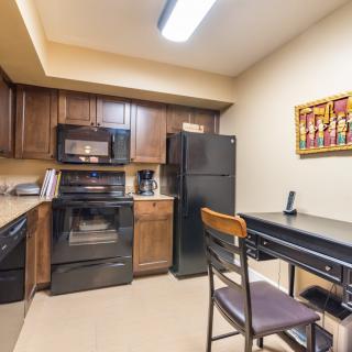 A cozy kitchen with dark wooden cabinets and black appliances, featuring a small dining table and colorful artwork on the wall.
