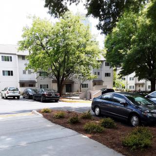A residential apartment complex with a parking lot and surrounding trees.