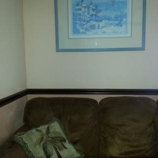 A cozy corner with a brown sofa, accented by a decorative pillow and a framed painting on the wall.