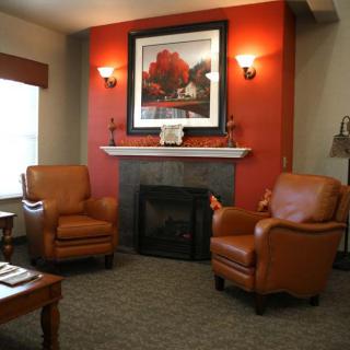 A cozy living room featuring leather armchairs and a fireplace, adorned with a vibrant painting and warm lighting.