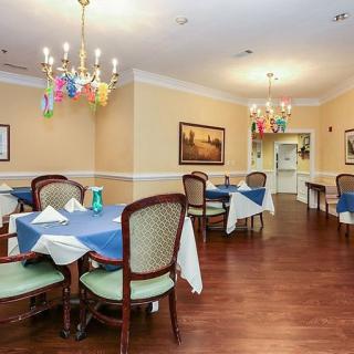 A neatly arranged dining room with tables covered in blue tablecloths, decorated chandeliers, and wooden flooring.