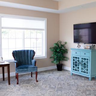 A cozy living room with a blue chair, ornate cabinet, and large window.
