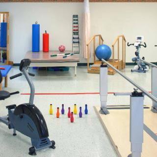 A well-equipped rehabilitation room with various exercise equipment, including an exercise bike, parallel bars, and therapy mats.