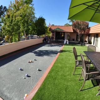 A sunny outdoor space with a bocce court, patio seating and green umbrellas surrounded by trees.