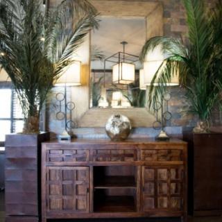 A stylish living room interior featuring a wooden sideboard, decorative plants, lamps, and a large mirror.
