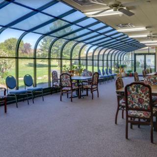 A sunlit conservatory with tables and chairs overlooking a green outdoor area.