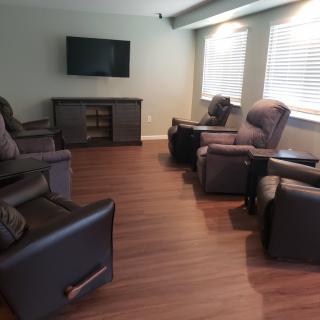 A cozy living room with several recliners arranged in a semi-circle facing a television.