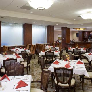 An elegant restaurant dining area with neatly arranged tables and chairs, featuring red napkins and soft lighting.
