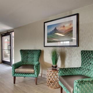 A cozy seating area with two green armchairs, a small table with a plant, and a framed landscape artwork on the wall.