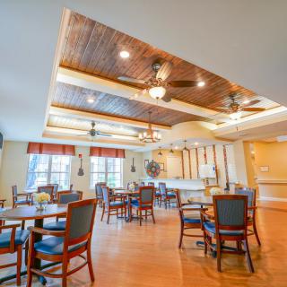 A spacious dining area with ceiling fans and wooden floors, featuring neatly arranged tables and chairs.