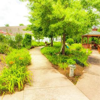A serene garden with a winding pathway bordered by lush greenery and a gazebo in the background.