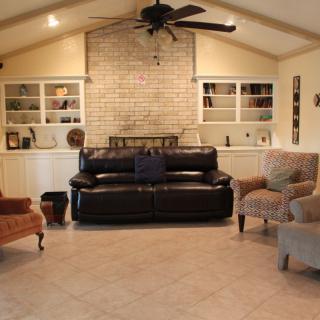 A cozy living room with a black leather sofa, patterned chairs, and built-in bookshelves flanking a brick accent wall.