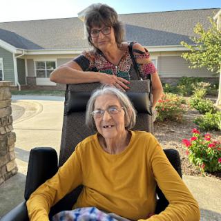 A warm moment shared between a caregiver and an elderly woman enjoying a sunny day outside.