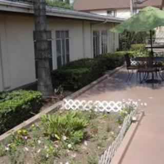 A peaceful patio area with a garden bed filled with flowers and outdoor seating under a green umbrella.