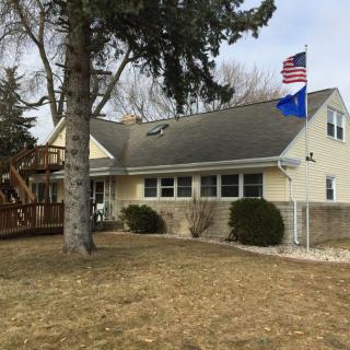 A residential house with a well-kept yard, featuring two flags on the roof and surrounded by trees.