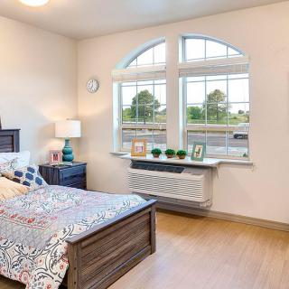 A cozy bedroom with a large window, featuring a neatly made bed and stylish decor.