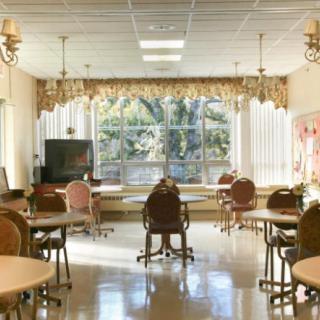 A bright and airy room with tables and chairs, featuring large windows allowing sunlight to stream in.