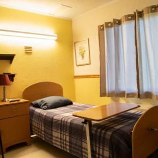 A simple and well-lit hospital room with a single bed, desk, and lamp.