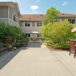 A sunny courtyard with outdoor seating, surrounded by lush greenery and apartment buildings.