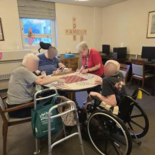 Elderly residents engage in a group activity with the assistance of a caregiver.