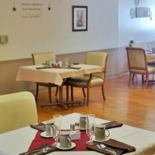 A neatly set dining room with tables and chairs, showcasing elegant table settings with silverware and cups.