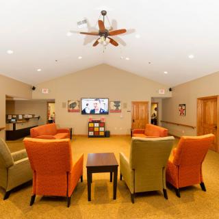 A cozy living room with colorful armchairs arranged facing a television, under a ceiling fan.