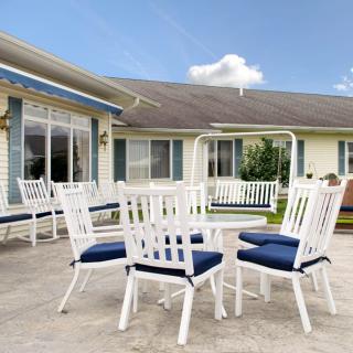 An inviting outdoor patio area featuring white chairs with blue cushions, a matching table, and a swing set against a house backdrop.