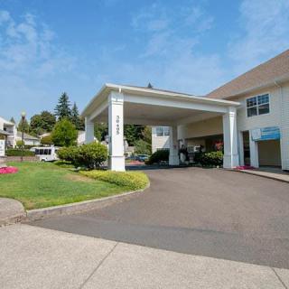 A building with a covered entrance and landscaped surroundings on a sunny day.