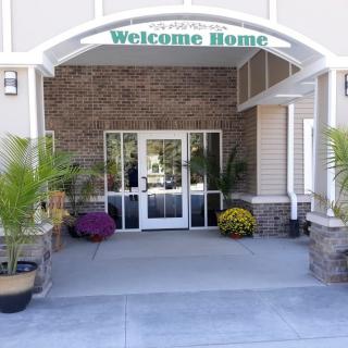 A welcoming building entrance adorned with potted plants and a 'Welcome Home' sign.