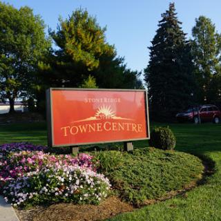 A welcoming sign at Towne Centre, surrounded by vibrant flowers and lush greenery.