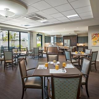 A modern dining room with neatly arranged tables and chairs, featuring ample natural light from large windows.
