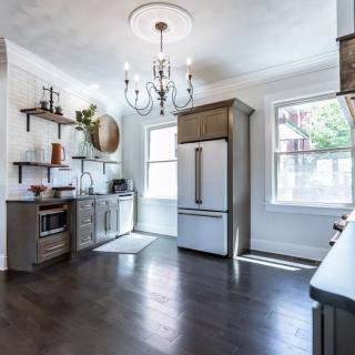A modern kitchen with a chandelier, featuring wood flooring, open shelving, and abundant natural light.