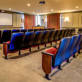 An empty theater-style conference room with arranged seating and a projector screen.