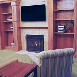 A cozy living room setup featuring a fireplace, flat-screen TV mounted above, and built-in wooden shelves.