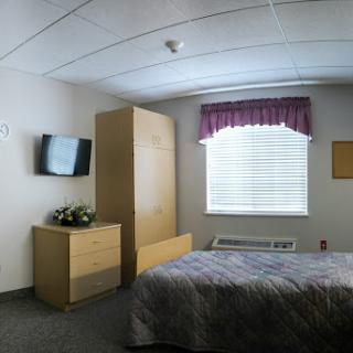 A cozy hotel room featuring a bed, television, and natural light coming through the window.