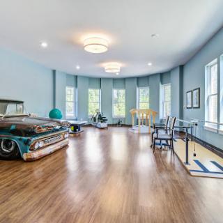 A spacious room featuring light blue walls and a vintage car, complemented by modern furnishings and ample natural light.