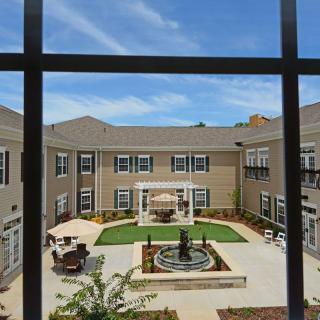 A view of a courtyard with a fountain and seating area surrounded by multi-story buildings under a clear blue sky.