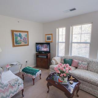 A cozy living room with a sofa, chairs, a coffee table adorned with flowers, and a television.