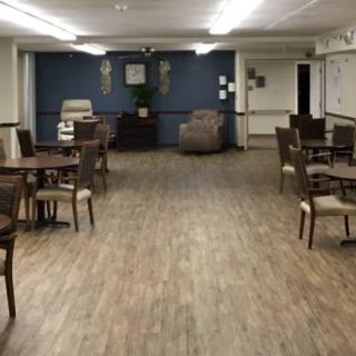 A spacious dining area with wooden flooring and multiple tables and chairs.