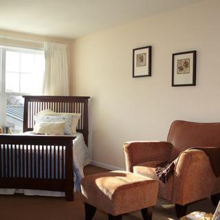 A cozy bedroom with an armchair and a neatly made bed by the window.