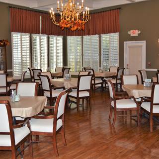 An elegant dining room with several tables and chairs, featuring a chandelier and wooden floors.
