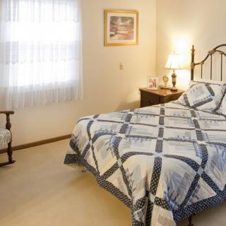 A cozy bedroom with a neatly made bed, a nightstand with a lamp, and natural light coming through the window.