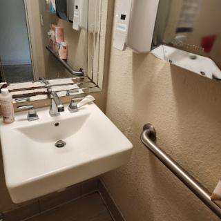 A well-maintained bathroom featuring a sink, mirror, and accessible handrail.