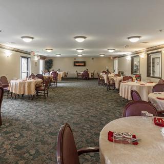 A spacious banquet hall with round tables and chairs arranged neatly, featuring a carpeted floor and ceiling lights.