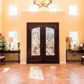 A spacious entryway featuring elegant double doors with wrought iron designs, complemented by side tables and decorative accents under a stylish lighting fixture.