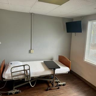 An empty hospital room with a single bed, a television on the wall, and a window providing natural light.