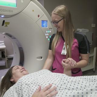 A nurse assists a patient preparing for a CT scan in a hospital setting.