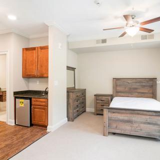 A modern bedroom with wooden furniture and a mini fridge.